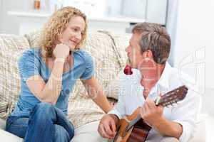 Romantic man playing guitar for her wife at home