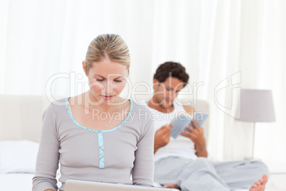 Woman working on her laptop while her husband is reading