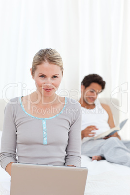 Woman working on her laptop while her husband is reading