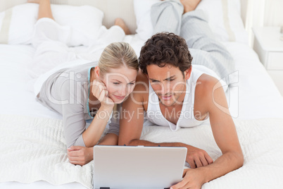 Adorable couple looking at their laptop on the bed