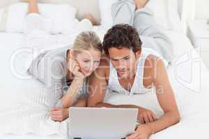 Adorable couple looking at their laptop on the bed