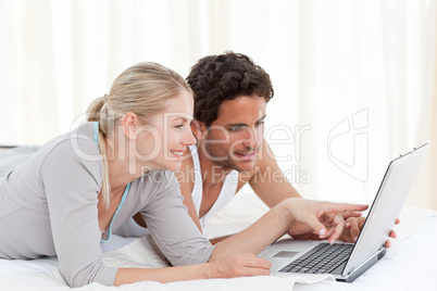 Adorable couple looking at their laptop on the bed