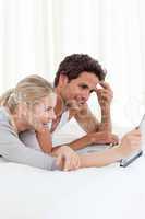 Adorable couple looking at their laptop on the bed