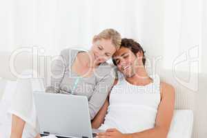 Adorable couple looking at their laptop on the bed