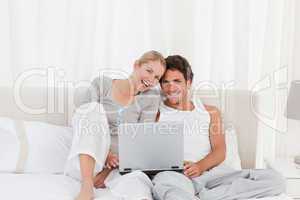 Adorable couple looking at their laptop on the bed