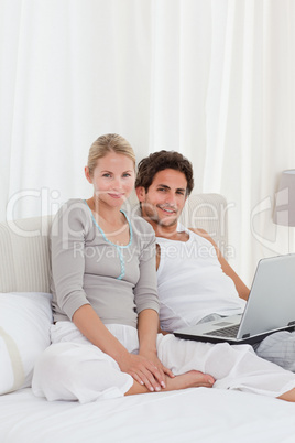 Adorable couple looking at their laptop on the bed