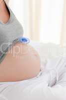 Pregnant woman with a baby dummy on her belly at home