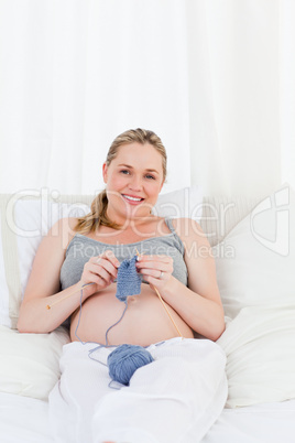 Adorable pregnant woman knitting on her bed