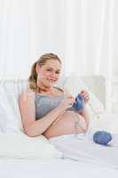 Adorable pregnant woman knitting on her bed