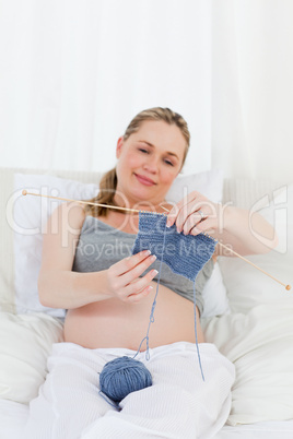 Adorable pregnant woman knitting on her bed