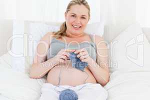 Adorable pregnant woman knitting on her bed