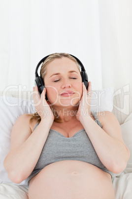 Lovely pregnant woman listening to music on her bed