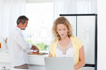 Woman working on her laptop while her husband is cooking