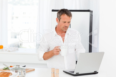 Man looking at his laptop while he is drinking