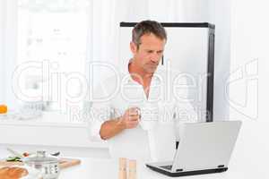 Man looking at his laptop while he is drinking