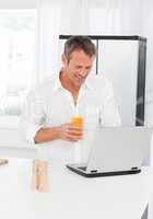 Man looking at his laptop while he is drinking oranje juice