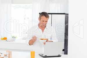 Man eating cereal while he is working on his laptop