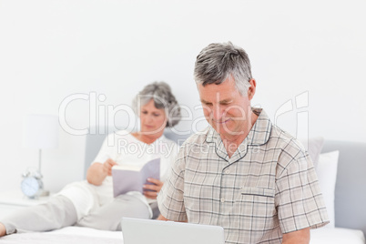 Man working on his laptop while his wife is reading