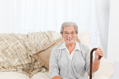 Mature woman sitting on the sofa with her walking stick