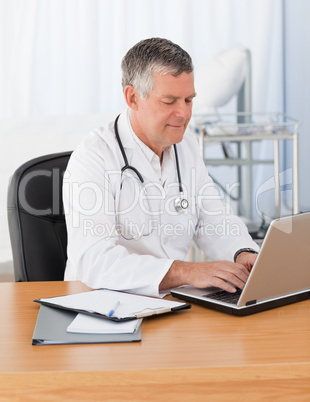 A senior doctor working on his laptop in his office