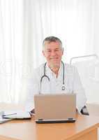 A senior doctor working on his laptop in his office