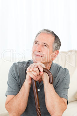 Mature man thoughtful with his walking stick on his bed