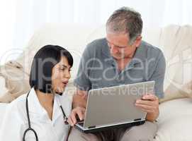 Mature man with his nurse looking at the laptop at home