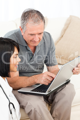 Mature man with his nurse looking at the laptop at home