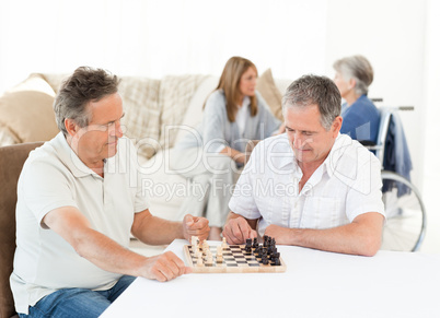 Men playing chess while their wifes are talking