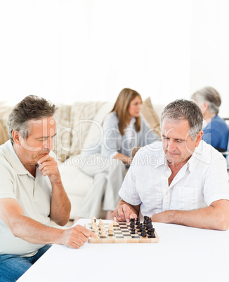 Men playing chess while their wifes are talking