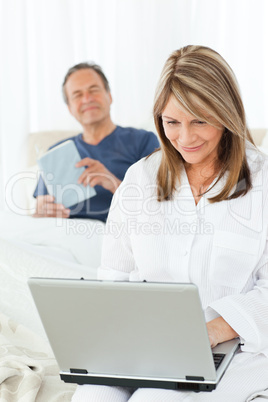 Woman looking at her laptop while her husband is reading