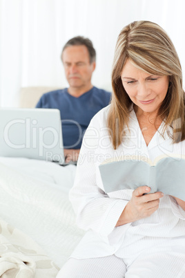 Man looking at his laptop while her wife is reading