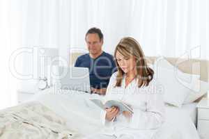 Senior  looking at his laptop while her wife is reading