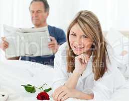 Happy woman with her rose while her husband is reading a newspap