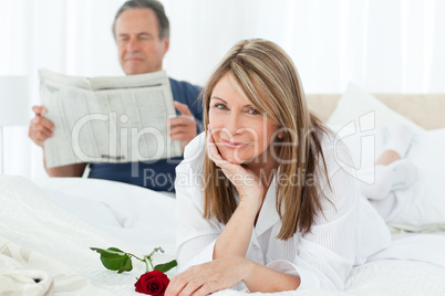 Happy woman with her rose while her husband is reading a newspap