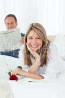 Happy woman with her rose while her husband is reading a newspap