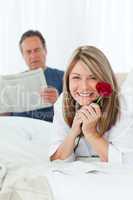 Happy woman with her rose while her husband is reading a newspap