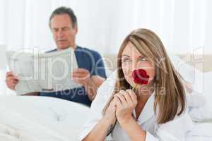 Happy woman smelling her rose while her husband is reading a new