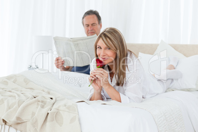 Happy woman with her rose while her husband is reading a newspap