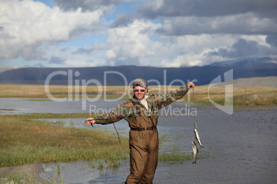 Fisherman with spinning catching fish in mountain lake Dayan Nuu