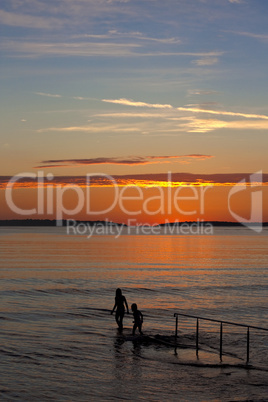 Two kids in sea with sunset