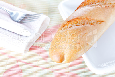 Baguette on white plate, napkin, fork and knife