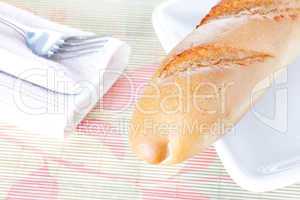 Baguette on white plate, napkin, fork and knife
