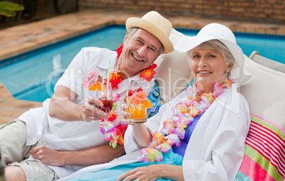 Mature couple drinking a cocktail  beside the swimming pool