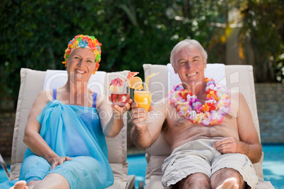 Mature couple drinking a cocktail  beside the swimming pool