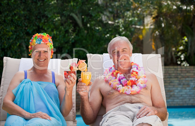 Mature couple drinking a cocktail  beside the swimming pool