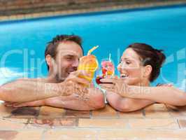 Beautiful couple drinking cocktails in the swimming pool