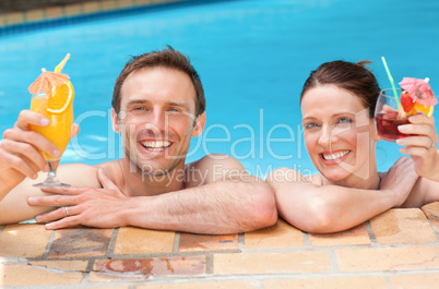 Beautiful couple drinking cocktails in the swimming pool