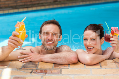 Beautiful couple drinking cocktails in the swimming pool