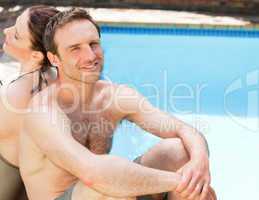 Couple sitting beside the swimming pool back to back